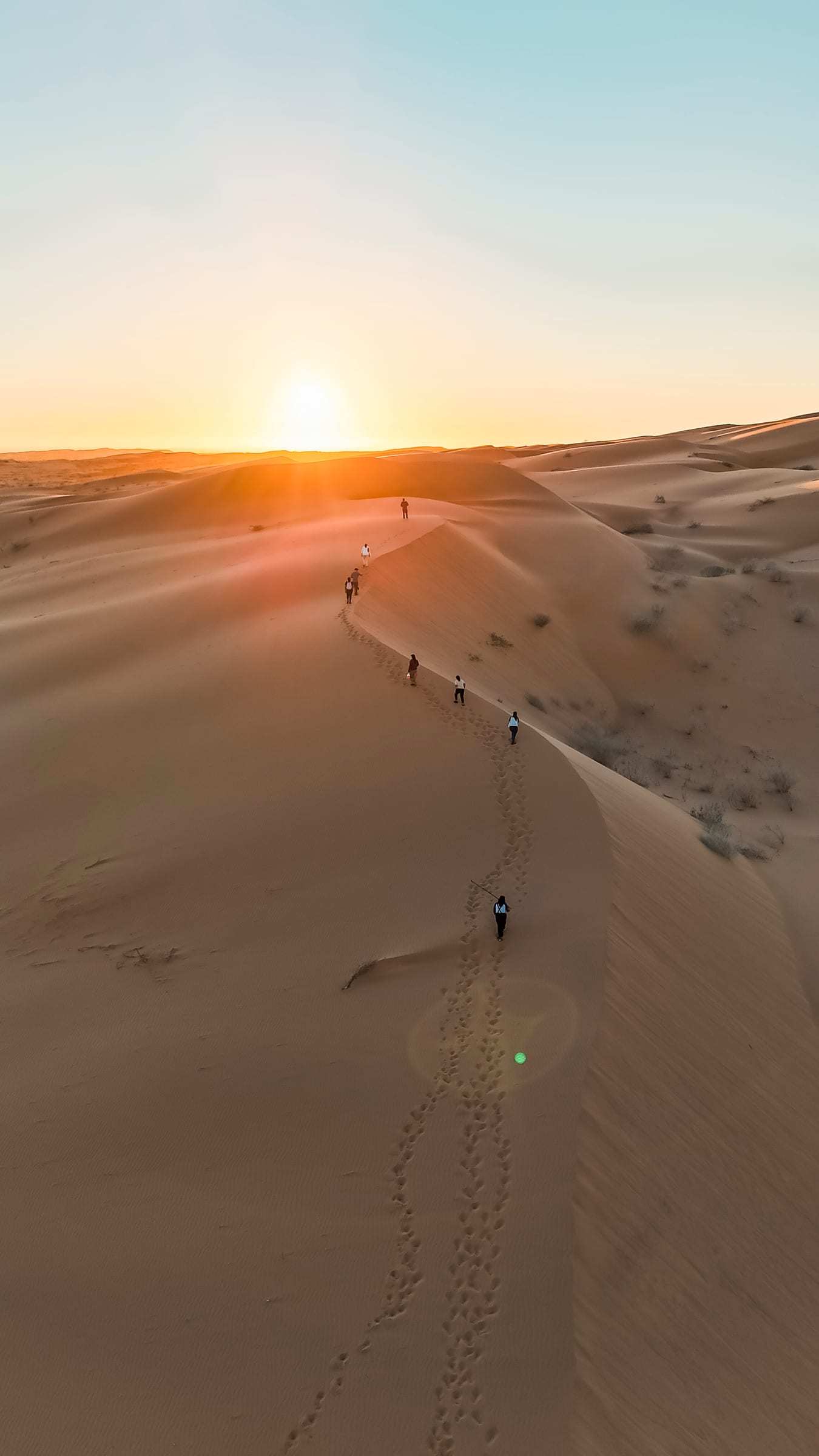 Fila de viajeros subiendo la cresta de una duna al atardecer