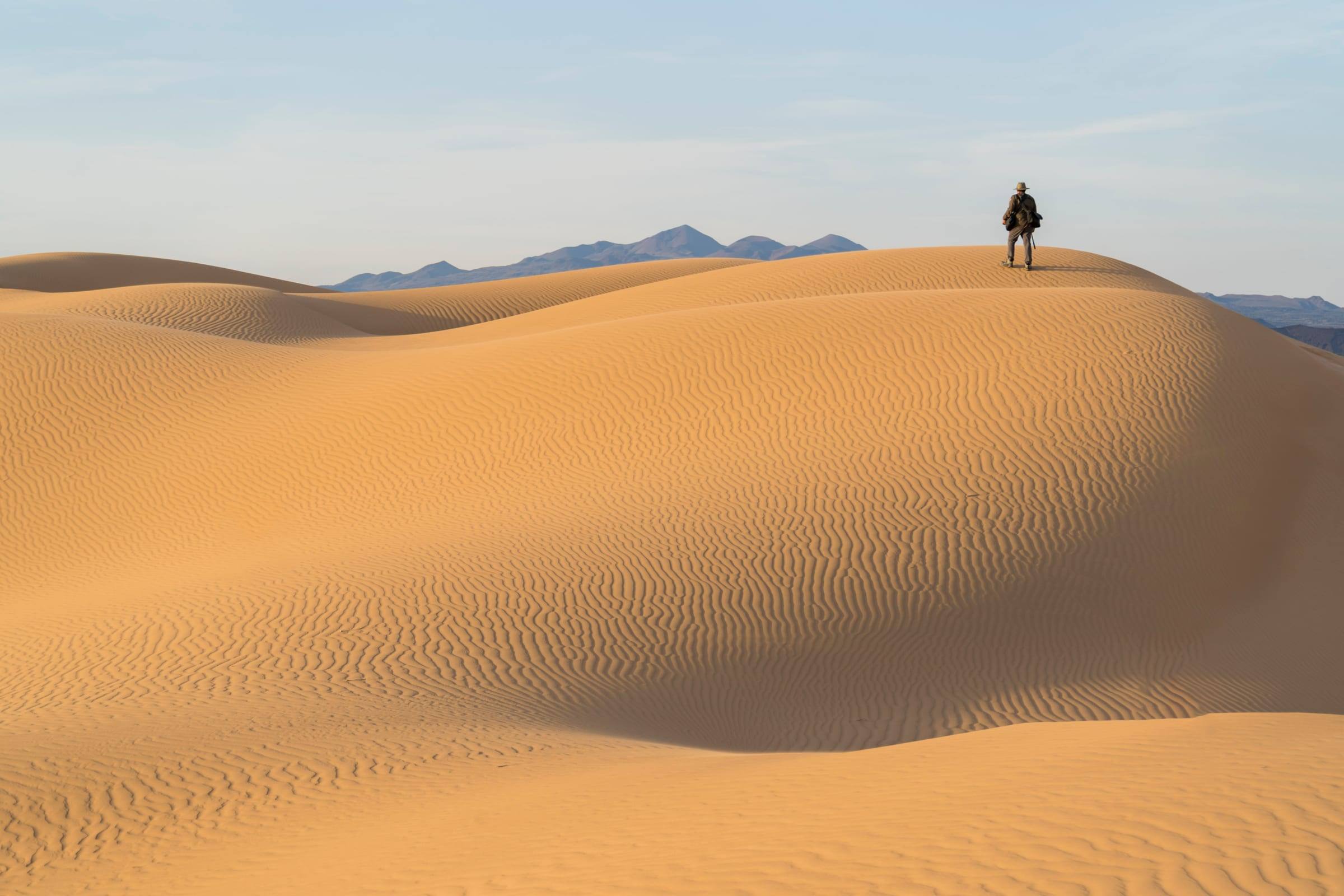 Un viajero camina por la cresta de las dunas del Gran Desierto de Altar, con la sierra al fondo