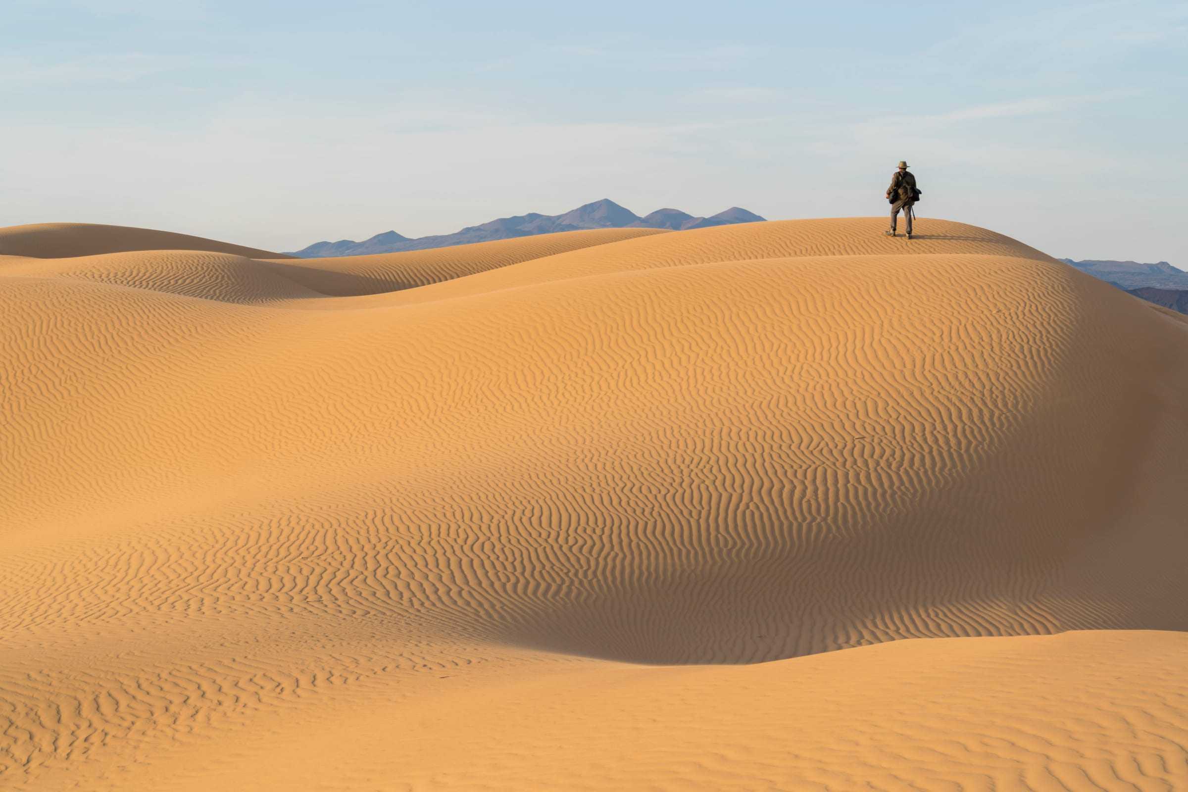Un viajero camina por la cresta de las dunas del Gran Desierto de Altar, con la sierra al fondo