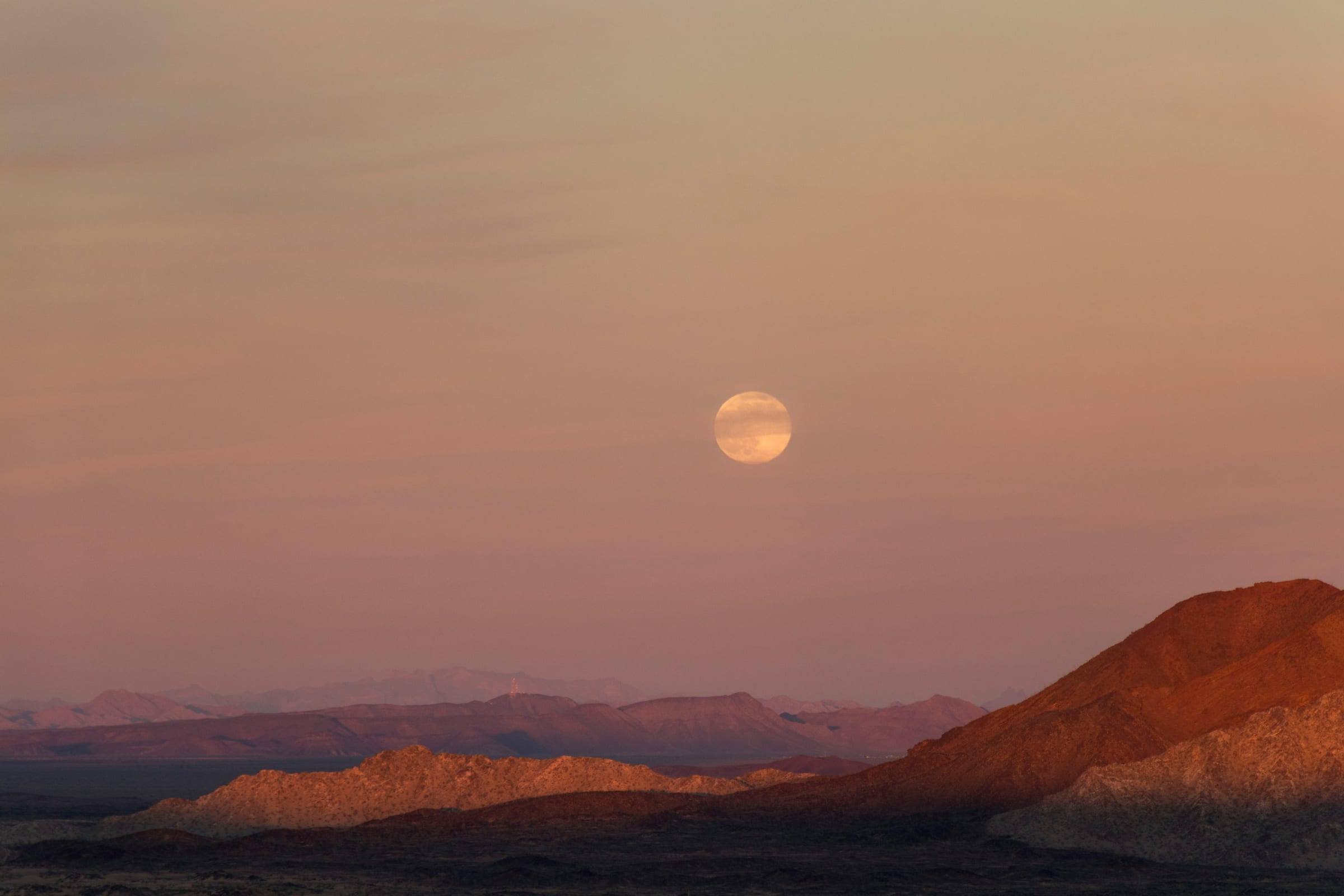 The full moon rising over the desert sierras at sunset