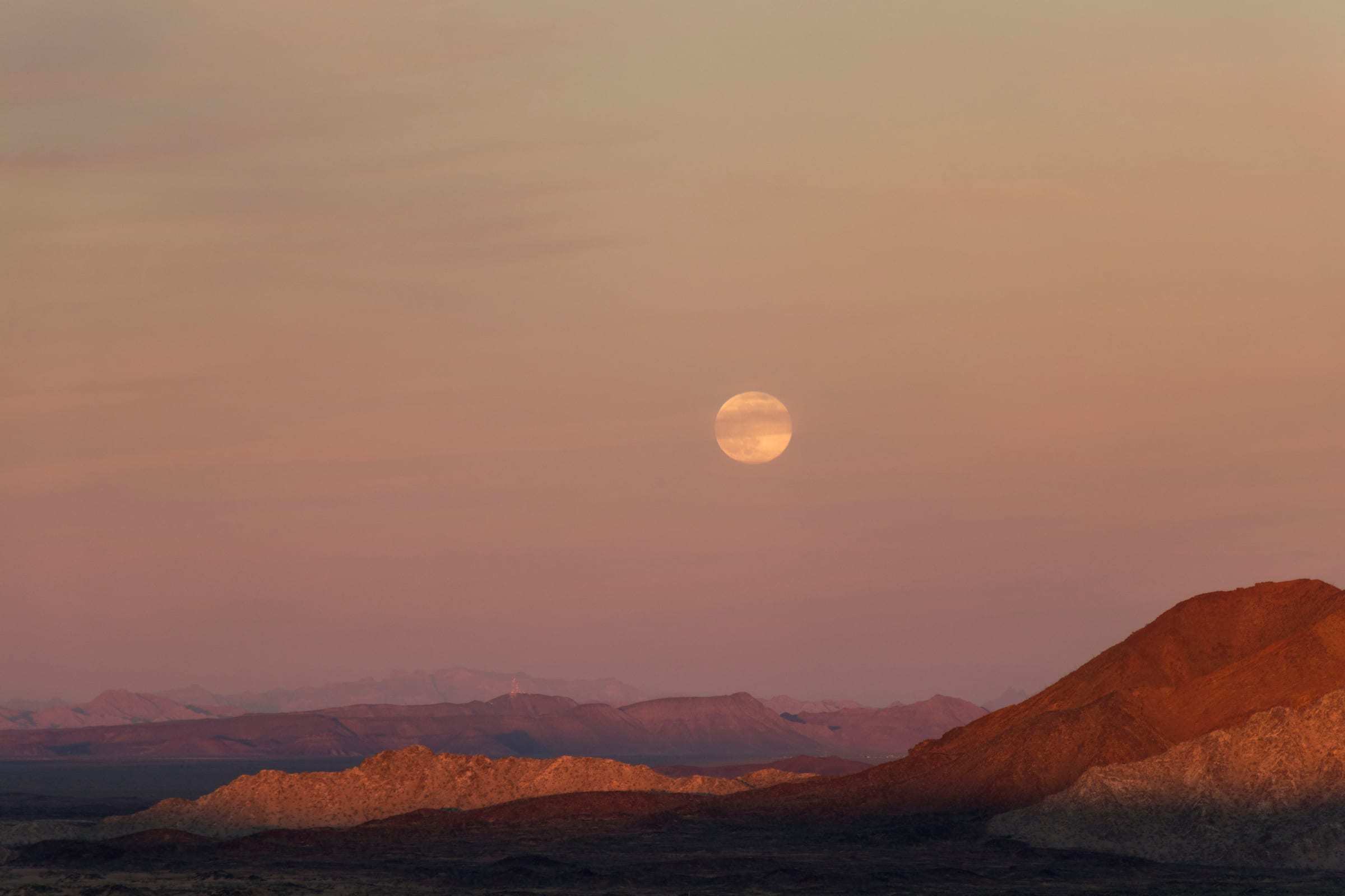 La luna llena saliendo sobre las sierras del desierto al atardecer