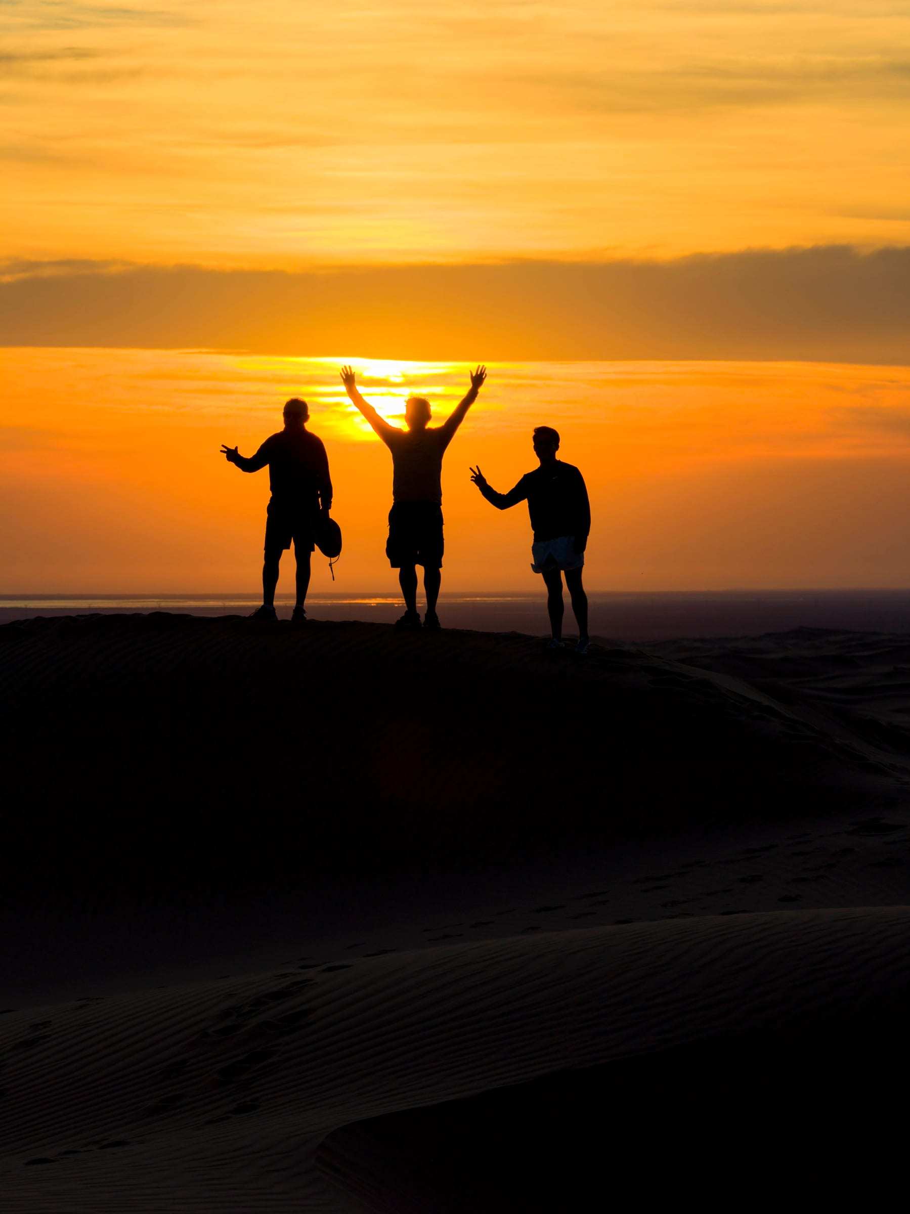 Tres viajeros en la cima de una duna, a contraluz del atardecer