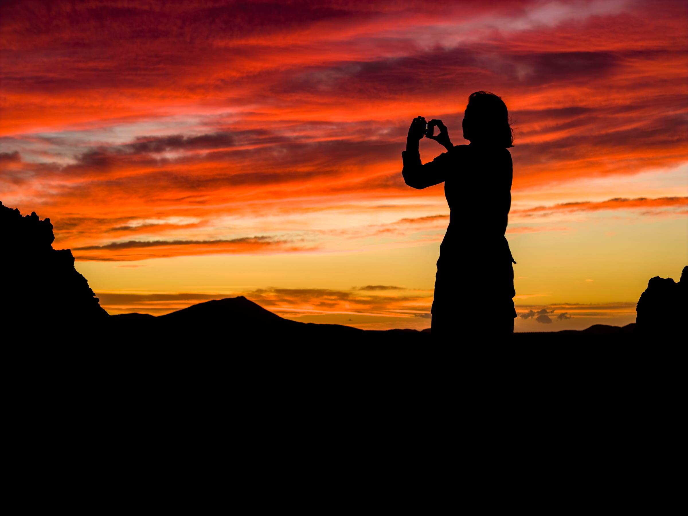 Silhouette d’une voyageuse photographiant le coucher du soleil sur la lave